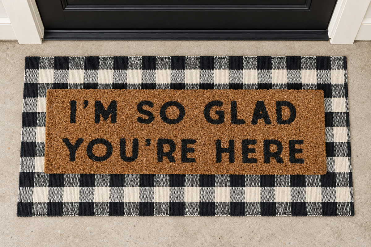XL Doormat | I'm So Glad You're Here layered over a black and ivory buffalo plaid runner at a black door.