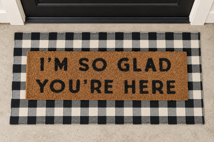XL Doormat | I'm So Glad You're Here layered over a black and ivory buffalo plaid runner at a black door.