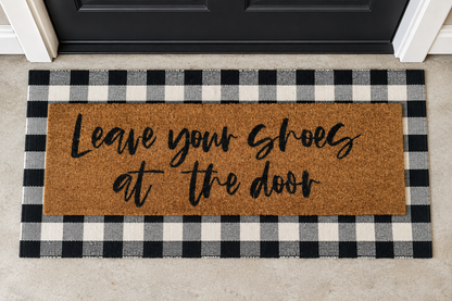 XL Doormat | Leave Your Shoes at the Door layered over a black and ivory buffalo plaid runner at a black door.