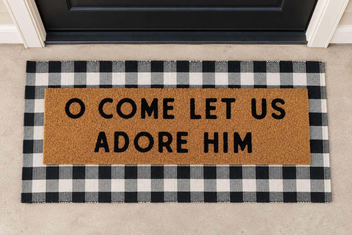 XL Christian Doormat | O Come Let Us Adore Him layered over a black and ivory buffalo plaid runner at a black door.