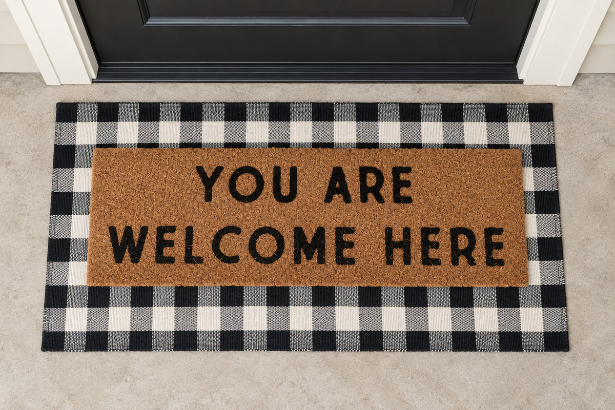 XL Doormat | You Are Welcome Here layered over a black and ivory buffalo plaid runner at a black door.