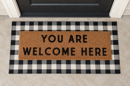 XL Doormat | You Are Welcome Here layered over a black and ivory buffalo plaid runner at a black door.