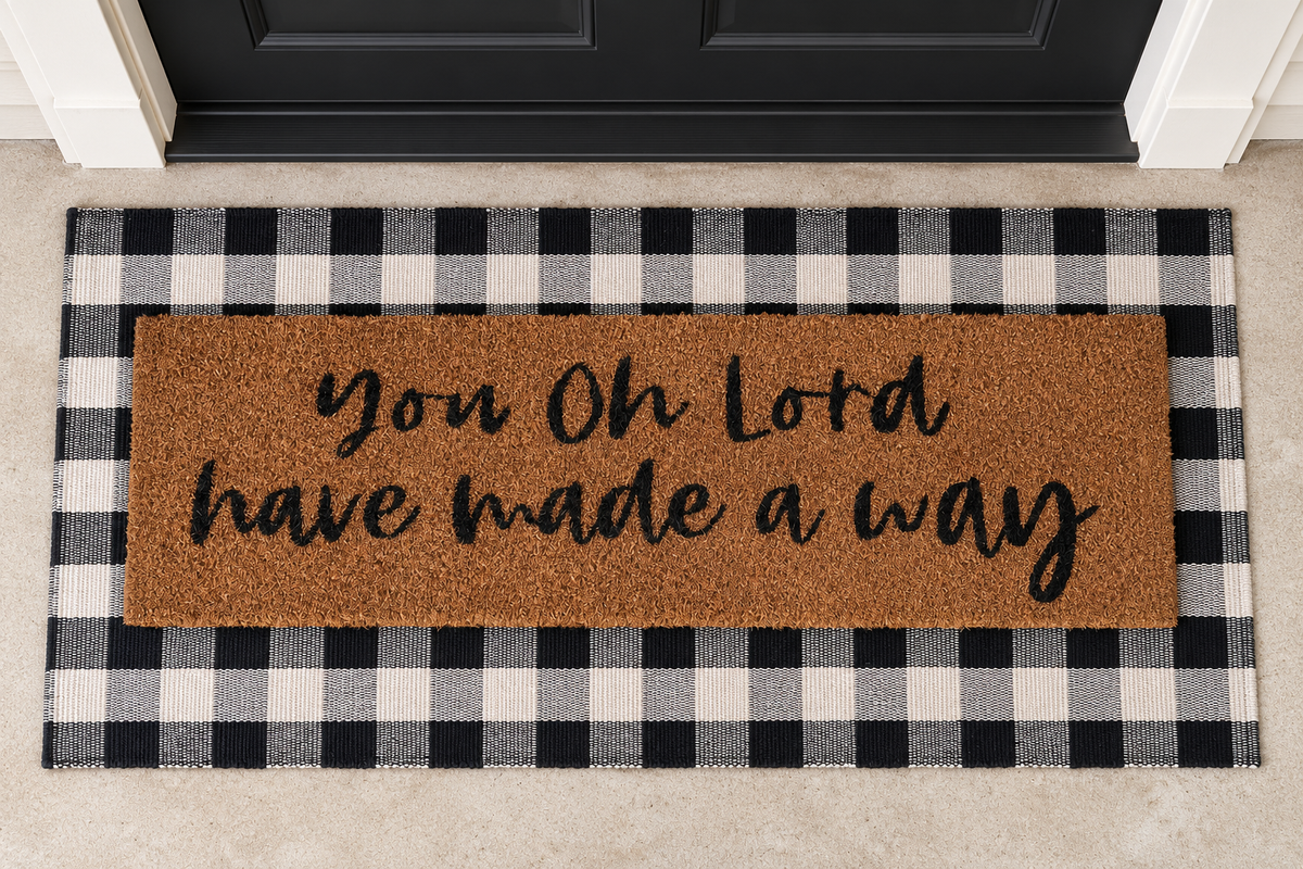 XL Christian Doormat | You, O Lord, Have Made a Way layered over a black and ivory buffalo plaid runner at a black door.