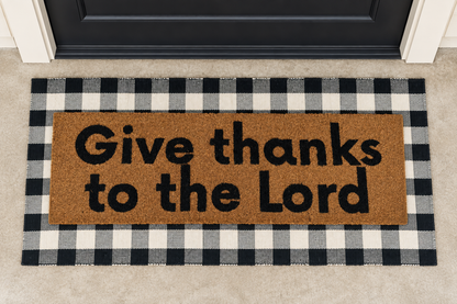 XL Christian Doormat | Give Thanks to the Lord layered over a black and ivory buffalo plaid runner at a black door.