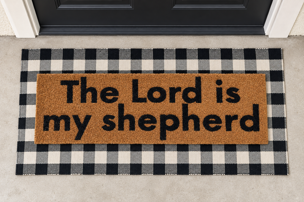 XL Scripture Doormat | The Lord Is My Shepherd layered over a black and ivory buffalo plaid runner at a black door.