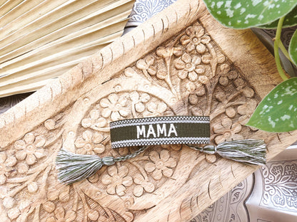Woven MAMA bracelet laid flat on a carved wooden tray, showing its band, cord closure and tassel ends.