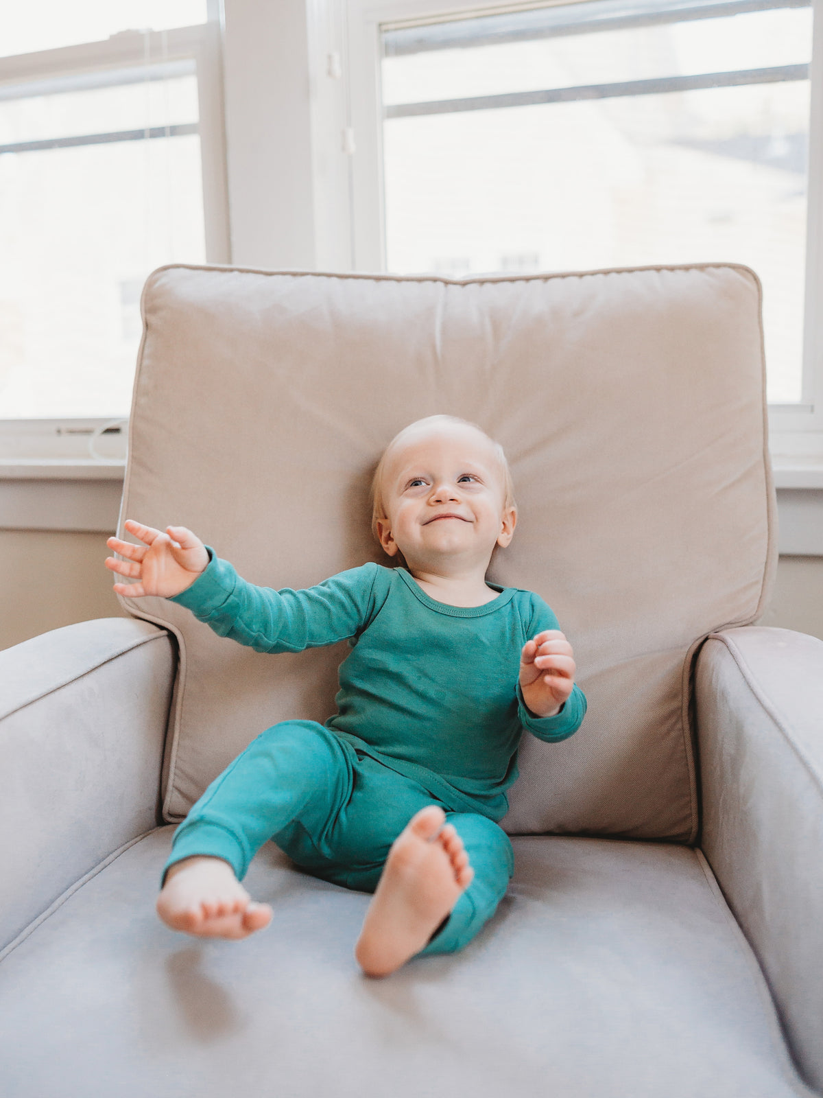Organic Baby + Kids Pajama Set | Pine Green — Baby wearing the set on an armchair