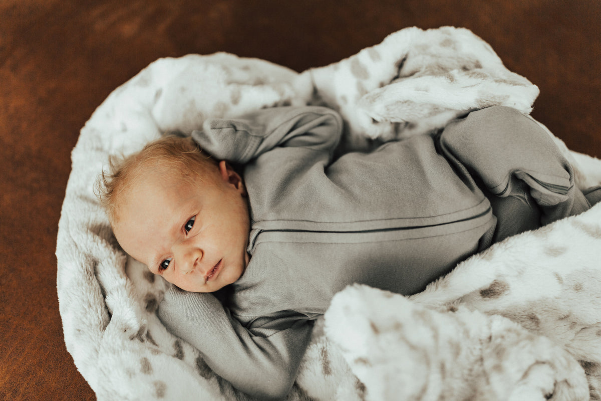 Close view of a baby in a gray footie, showing the front zipper and covered hands