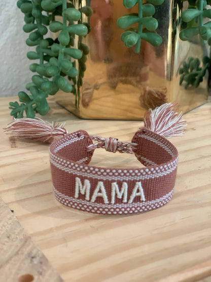 Rose-toned woven MAMA bracelet with pale embroidered lettering, a sliding cord closure and tassel ends.
