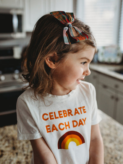 Close-up of a child wearing the Celebrate Each Day tee, showing the lettering and rainbow.
