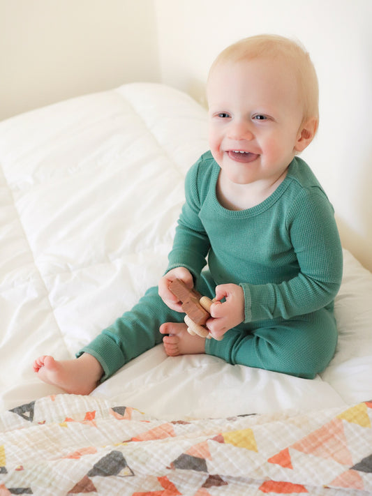 Baby seated on a bed wearing pine green thermal pajamas