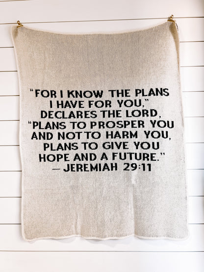 Natural Jeremiah 29:11 blanket with black block lettering, hanging against a white plank wall.