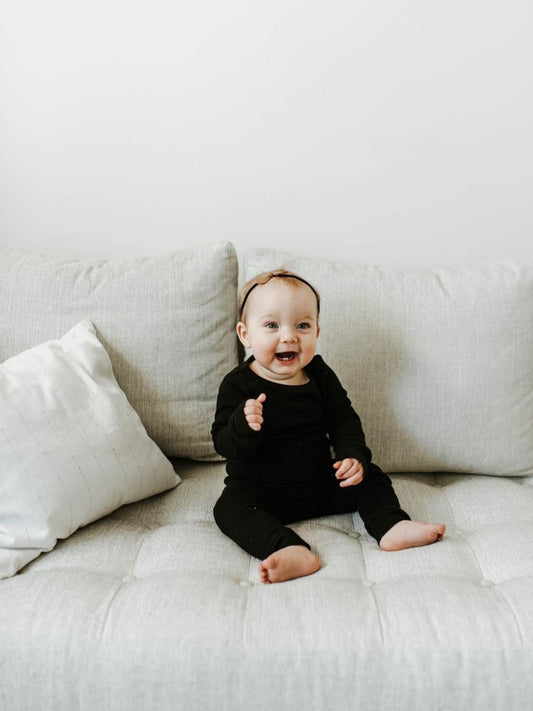 Baby wearing black pajamas seated on a white sofa