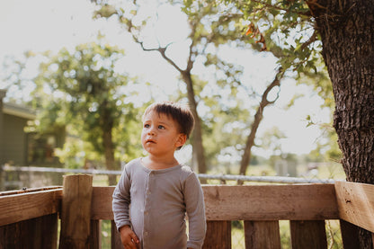 Child wearing a gray button coverall on a wooden porch