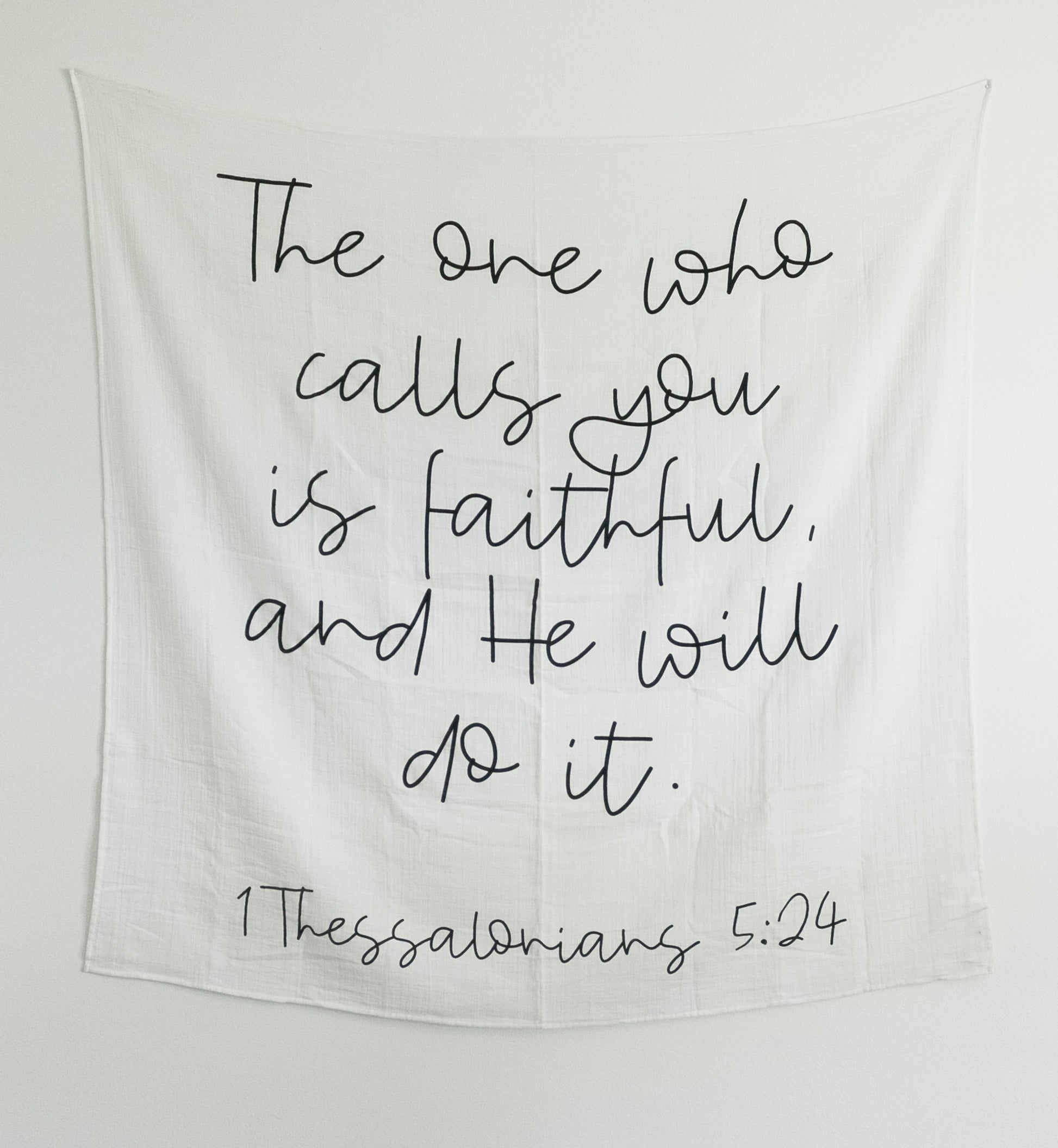 Black and white swaddle blanket with text printed on it, hanging on a wall as art, with a wooden box below containing what appears to be baby-related items.