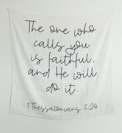 Black and white swaddle blanket with text printed on it, hanging on a wall as art, with a wooden box below containing what appears to be baby-related items.