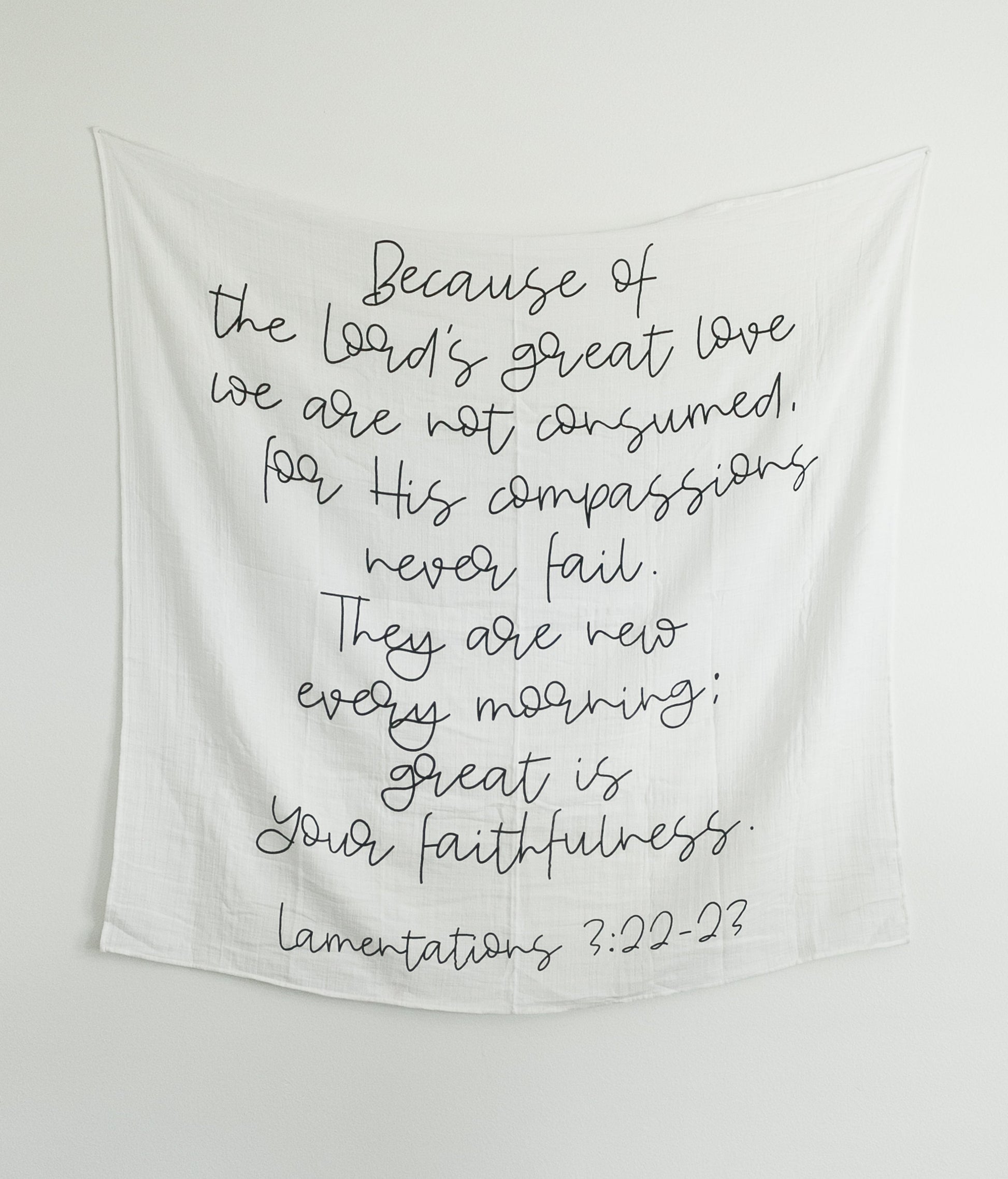 A black and white muslin swaddle blanket with text printed on it hanging on the wall, with a wooden box below.