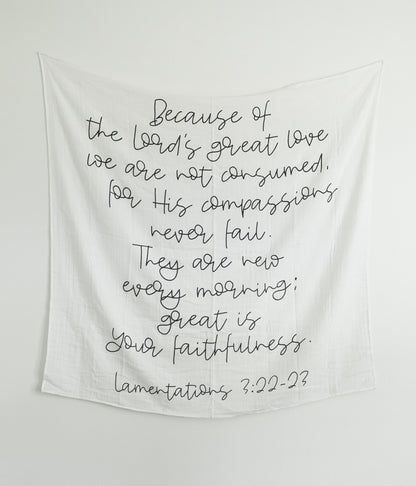 A black and white muslin swaddle blanket with text printed on it hanging on the wall, with a wooden box below.