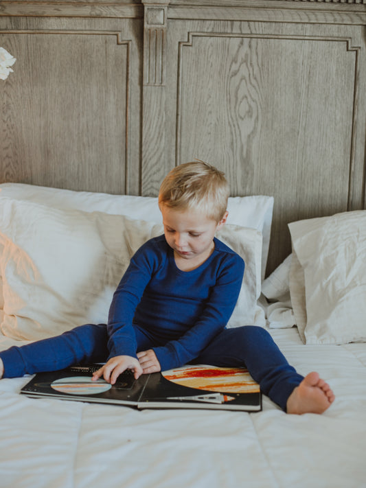 Child reading on a bed wearing navy blue thermal pajamas