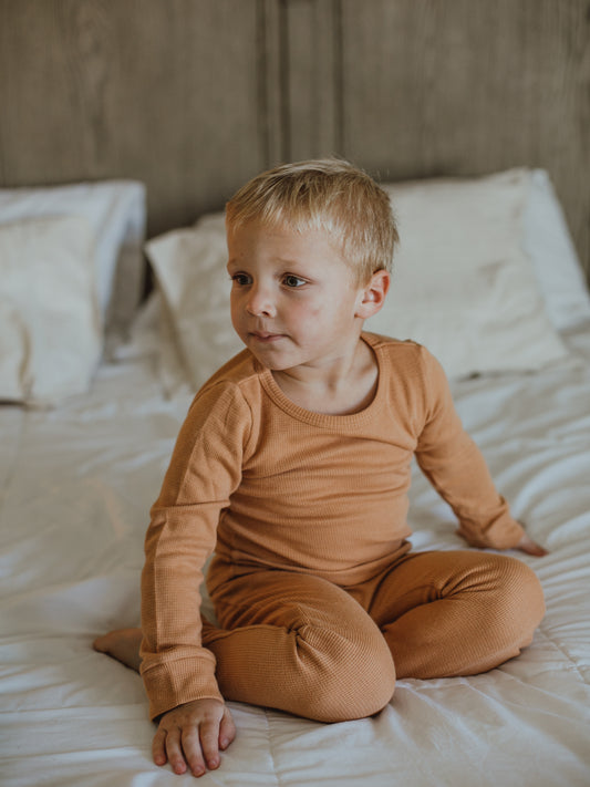 Child seated on a bed wearing ginger thermal pajamas