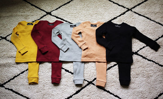 Two-piece pajama sets in assorted solid colors arranged on a patterned rug
