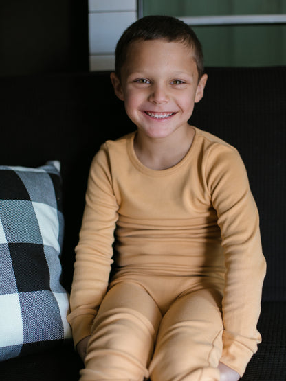 Organic Baby + Kids Pajama Set | Honey — Child seated in honey pajamas