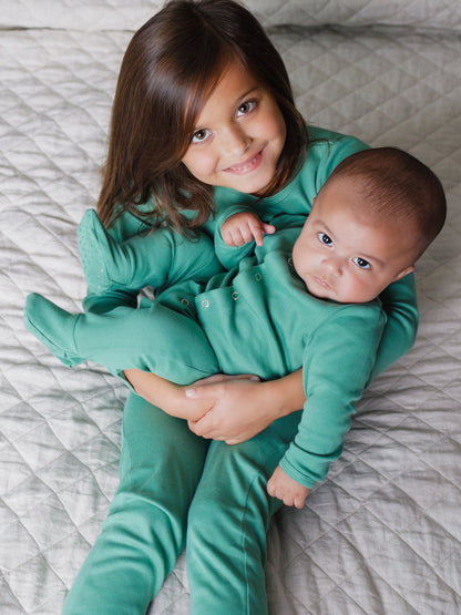 Organic Baby + Kids Pajama Set | Pine Green — Older child holding a baby in matching green pajamas