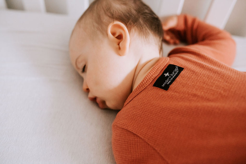 Close-up of the back neckline and label of a rust-colored thermal zip coverall worn by a baby.