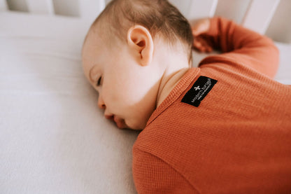 Close-up of the back neckline and label of a rust-colored thermal zip coverall worn by a baby.