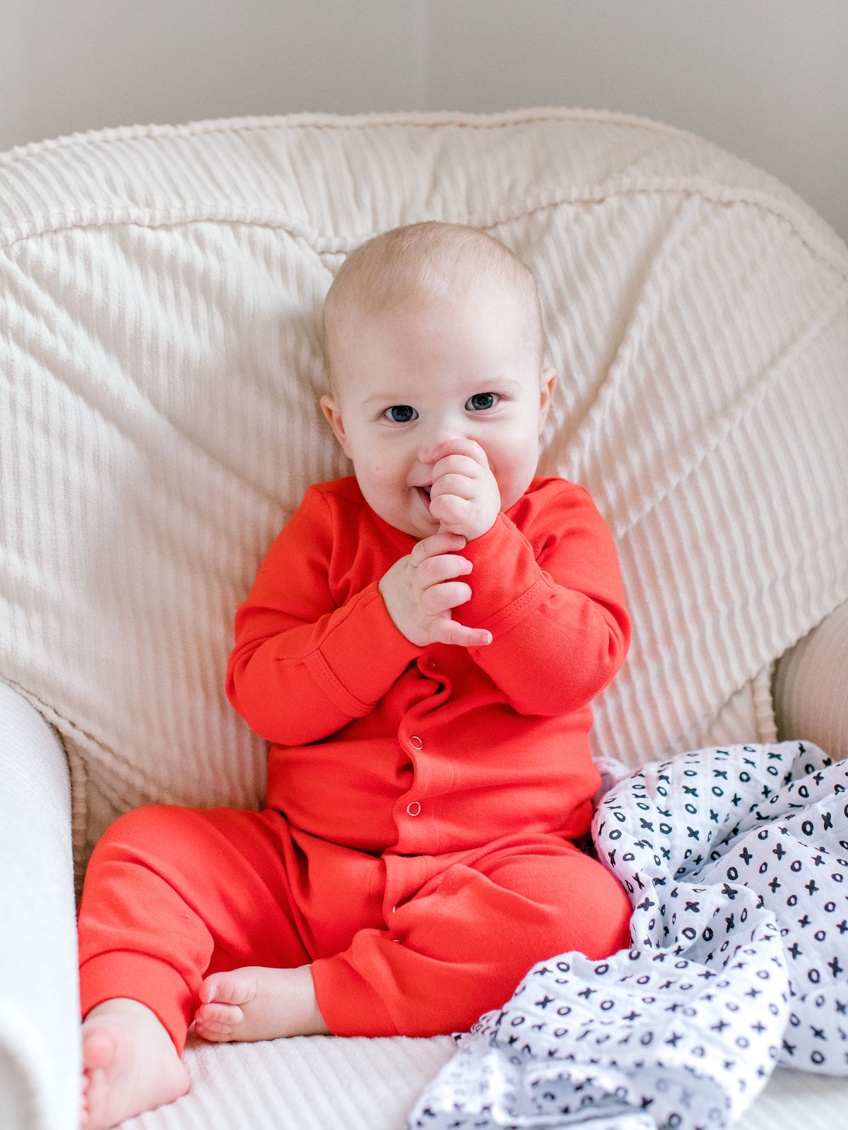 Baby seated in a bright red button coverall with bare feet
