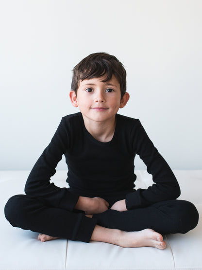 Organic Thermal Baby + Kids Pajama Set | Black — Child seated in the full black pajama set