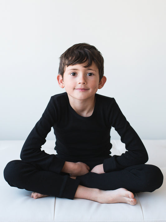 Child seated on a white sofa wearing black thermal pajamas