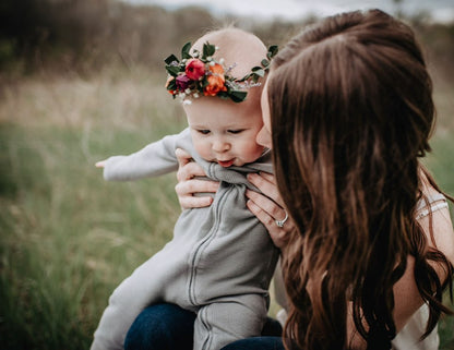 Adult holding a baby in a gray thermal zip coverall outdoors.