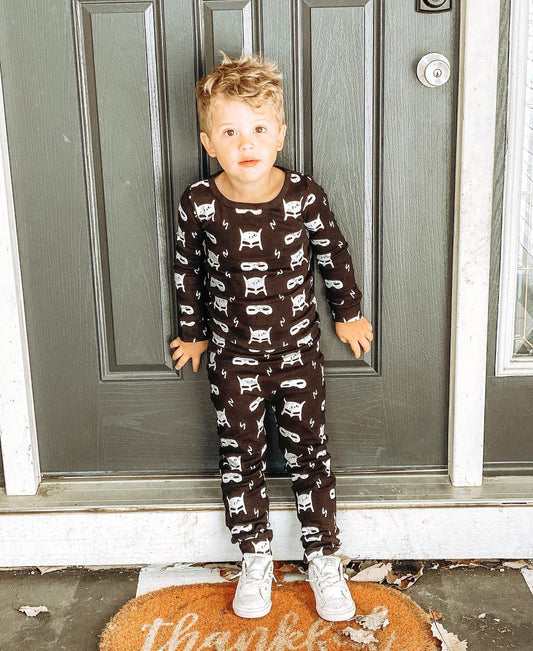 Child standing in a black pajama set with white superhero motifs