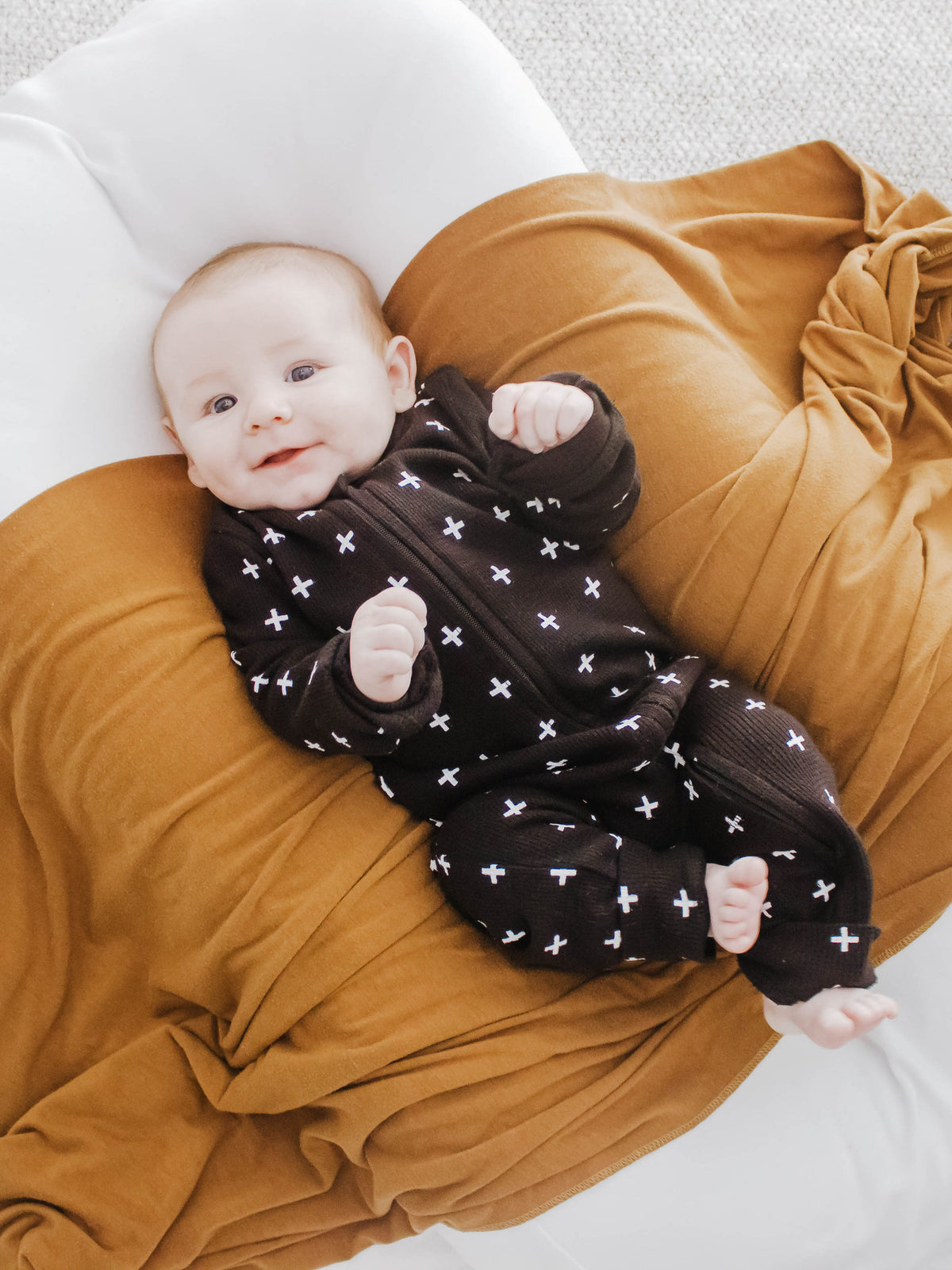 Baby wearing a black Swiss cross thermal zip coverall while resting in an adult's arms.