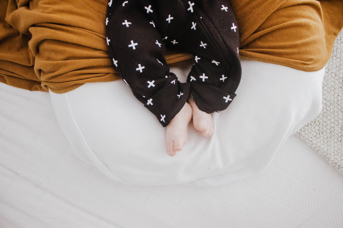 Close-up of the legs and ankle cuffs of a black Swiss cross thermal zip coverall worn by a baby.