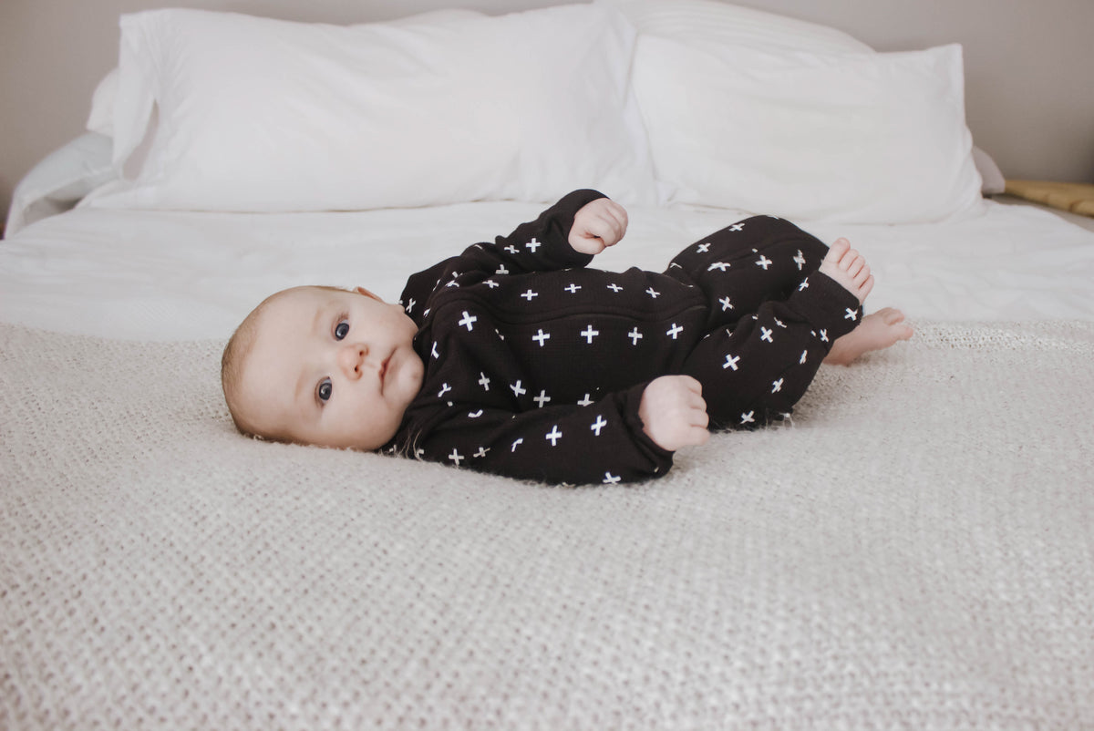 Baby lying on a bed wearing a black thermal zip coverall with white Swiss crosses.